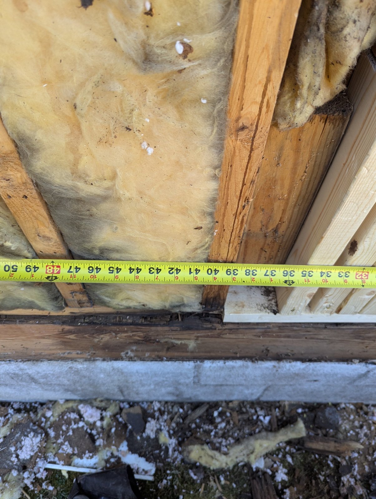 Damaged lower wall framing exposed beneath insulation